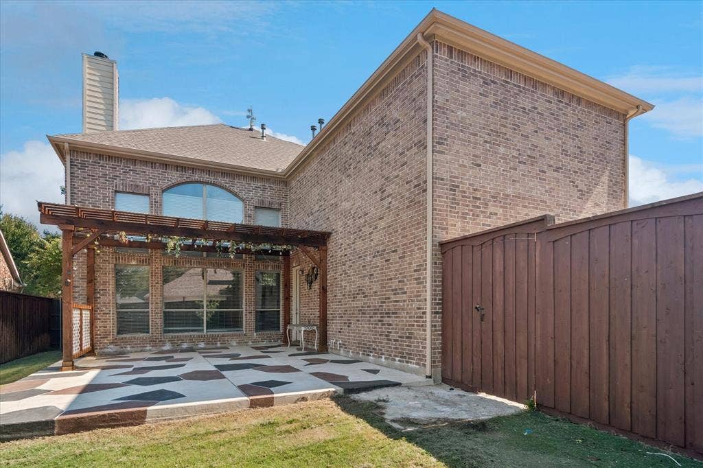 8323 Albritton Drive, Frisco, TX 75036 Brick exterior with a wood pergola, patterned concrete patio, full privacy fence, and large window openings