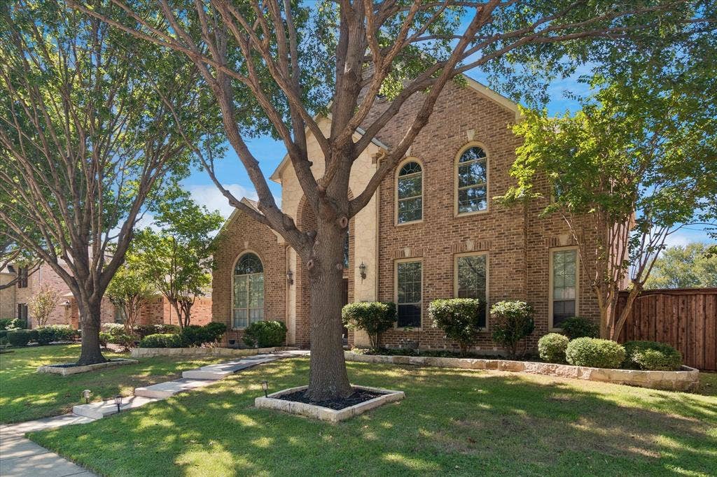 8323 Albritton Drive, Frisco, TX 75036 Brick facade with arched windows, mature trees, and stone-edged landscaping