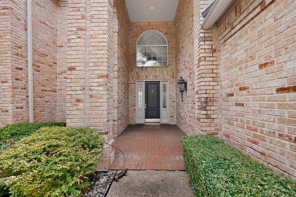 4536 Briar Oaks Circle, Dallas, TX 75287 Brick exterior with a covered entry, arched transom window, black paneled front door with sidelights, and a brick paver porch