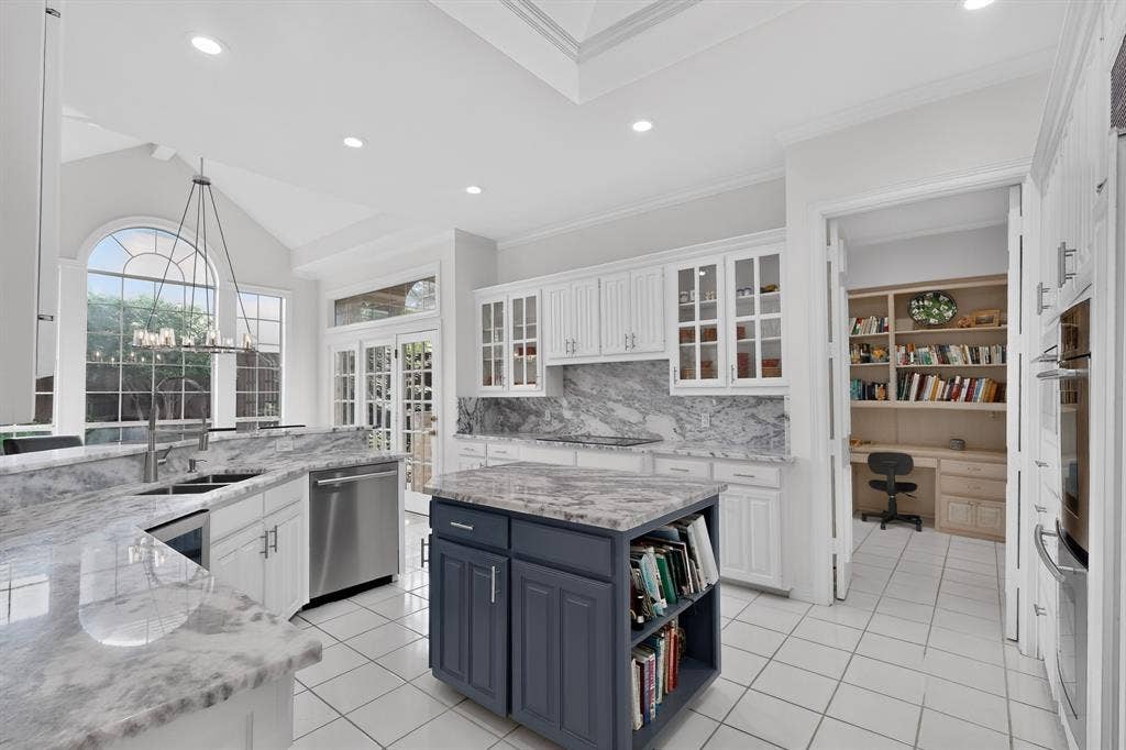 4536 Briar Oaks Circle, Dallas, TX 75287 Gourmet kitchen featuring white cabinetry, stone countertops, a central island with built-in shelving, stainless steel appliances, and a vaulted ceiling with an arched window