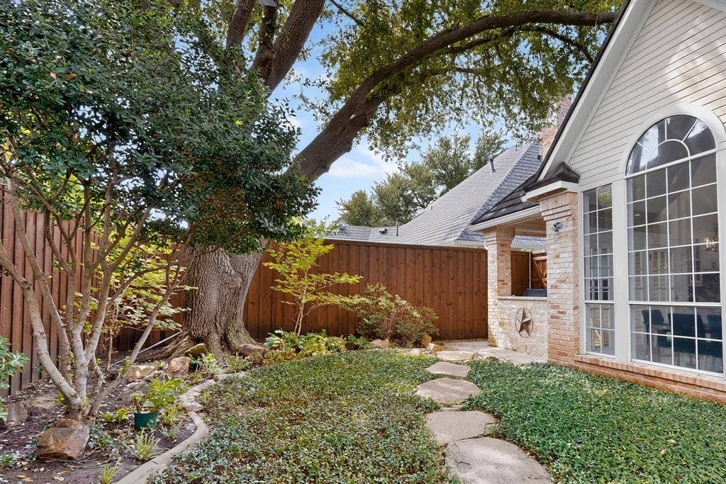 4536 Briar Oaks Circle, Dallas, TX 75287 Manicured landscaping with mature trees, stone pathway, brick exterior, arched window, and covered patio