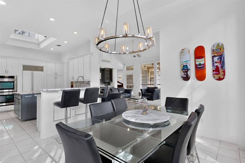 4536 Briar Oaks Circle, Dallas, TX 75287 Contemporary dining and kitchen showcase featuring a round glass-top dining table with black upholstered chairs, stainless steel appliances, white cabinetry with integrated refrigeration, light-filled layout with recessed ceiling lighting, and a modern pendant fixture with warm-toned accents