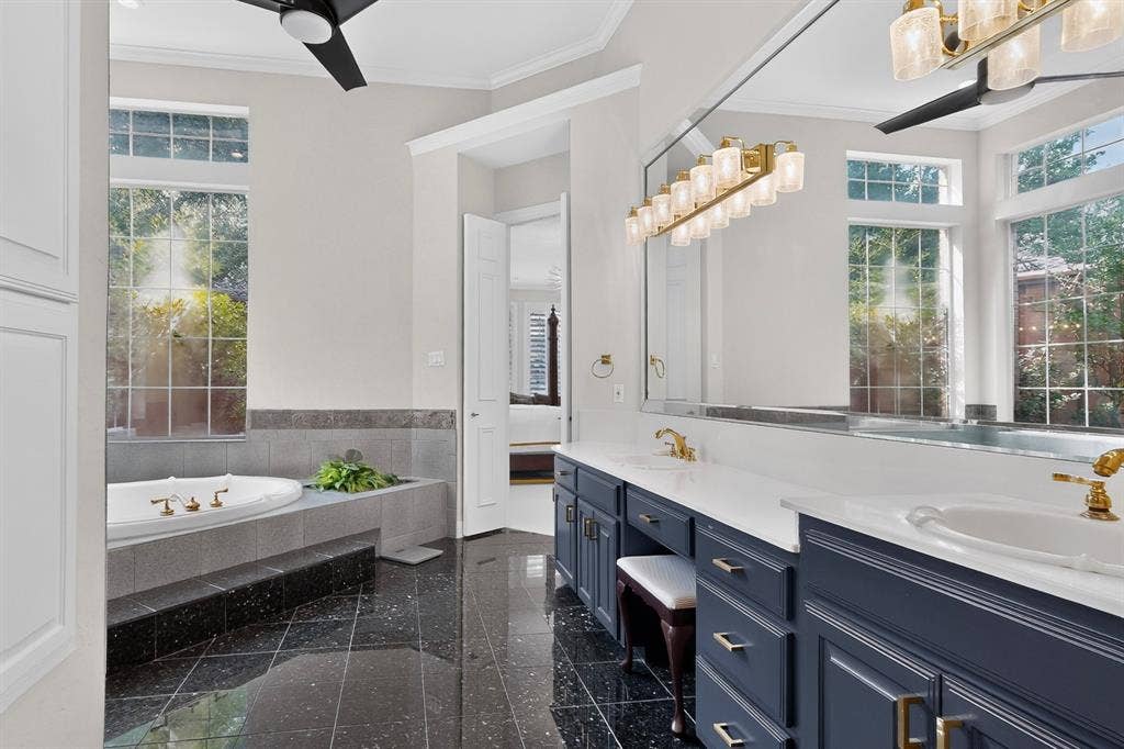4536 Briar Oaks Circle, Dallas, TX 75287 Soaking tub with surrounding tile, dual vanity with white countertops, black tile flooring, and two ceiling fans
