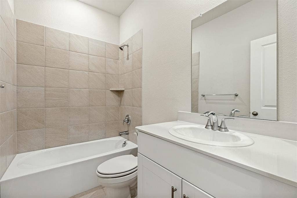 1006 Angel Street, Josephine, TX 75173 Fresh Finishes & Everyday Functionality! - The secondary bathroom features a white vanity with chrome fixtures, a spacious mirror, and a tub-shower combination with ceramic tile surround, offering a clean, contemporary look and practical convenience.