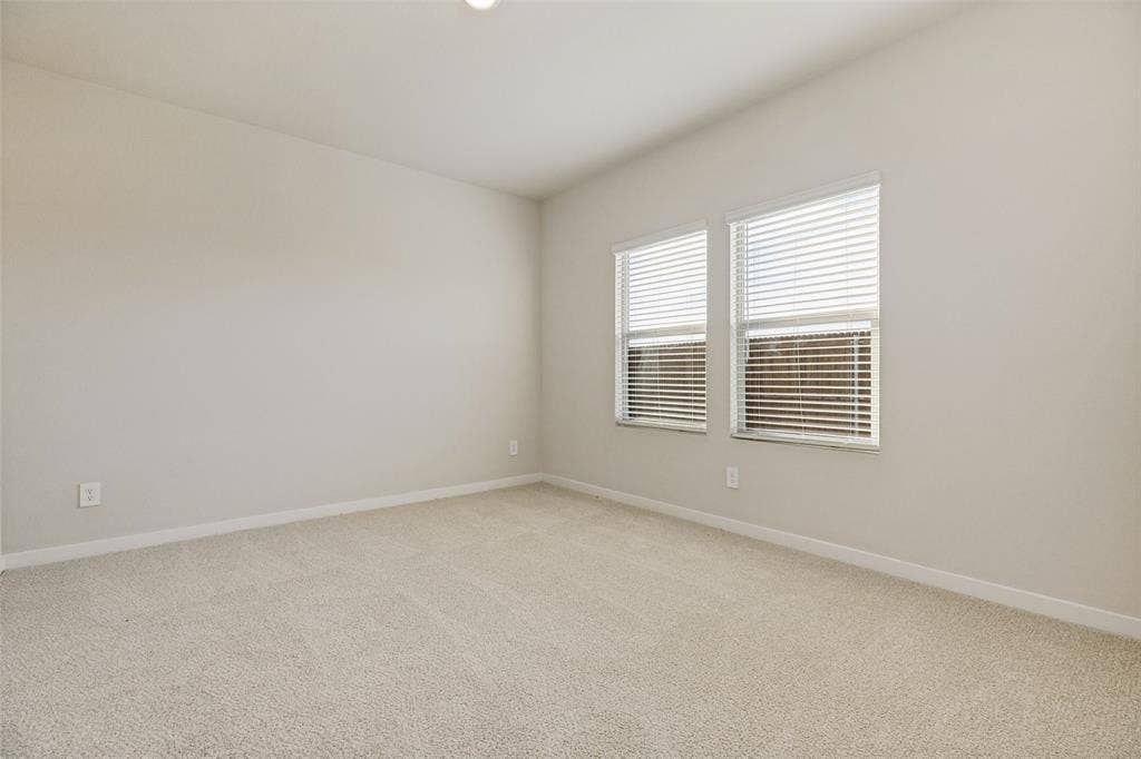 1006 Angel Street, Josephine, TX 75173 Your Own Comfortable Retreat! - The spacious primary bedroom offers plush neutral carpeting, soft natural light from two windows, and a peaceful atmosphere designed for relaxing and recharging at the end of the day.