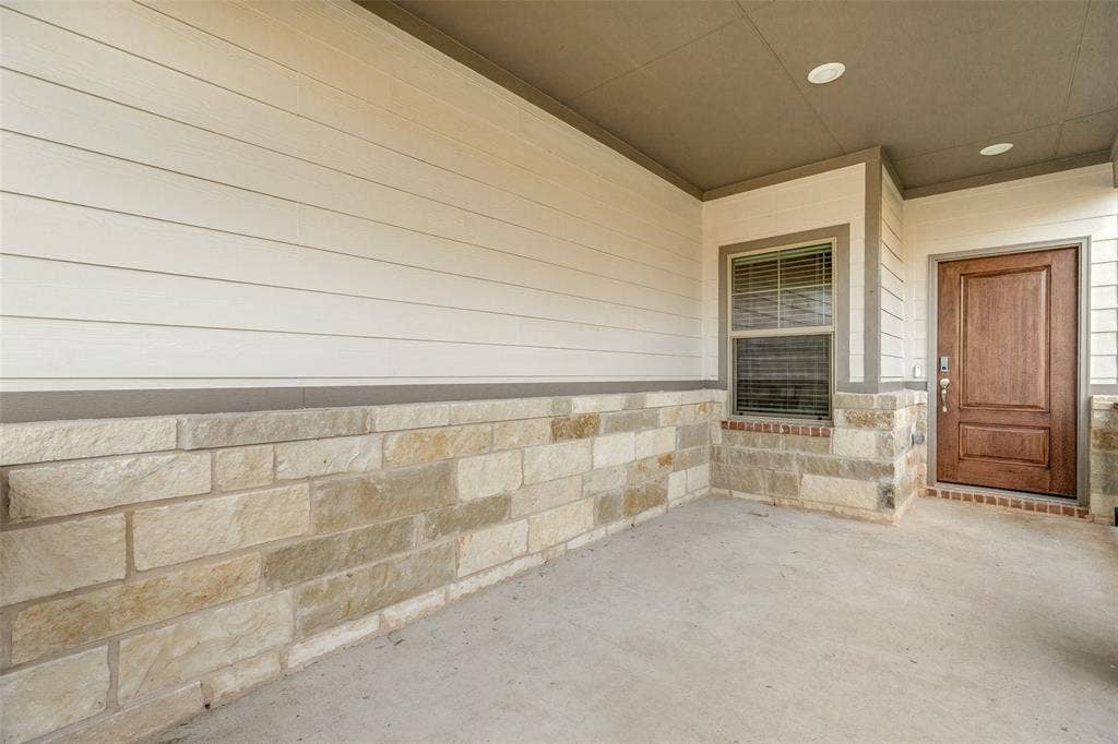1006 Angel Street, Josephine, TX 75173 A Front Porch Made for Relaxing! - The generously sized covered porch features beautiful stone accents, low-maintenance siding, recessed lighting, and a stained front door, creating a welcoming outdoor space to enjoy morning coffee or unwind in the evening.