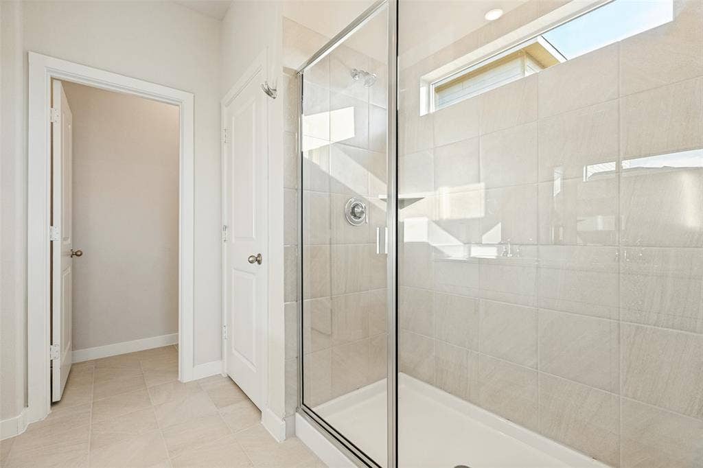 1006 Angel Street, Josephine, TX 75173 A Refreshing Start to Every Day! - The spacious walk-in shower features a ceramic tile surround, clear glass enclosure, chrome fixtures, and a high window that welcomes natural light while maintaining privacy.