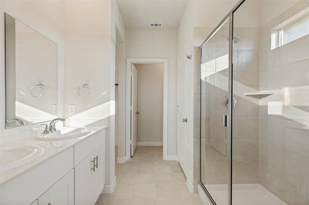 1006 Angel Street, Josephine, TX 75173 Fresh, Bright & Beautifully Functional! - The primary bathroom features a dual-sink vanity with white shaker-style cabinetry, sleek chrome fixtures, and a spacious glass-enclosed shower with ceramic tile surround. A private water closet adds everyday convenience.