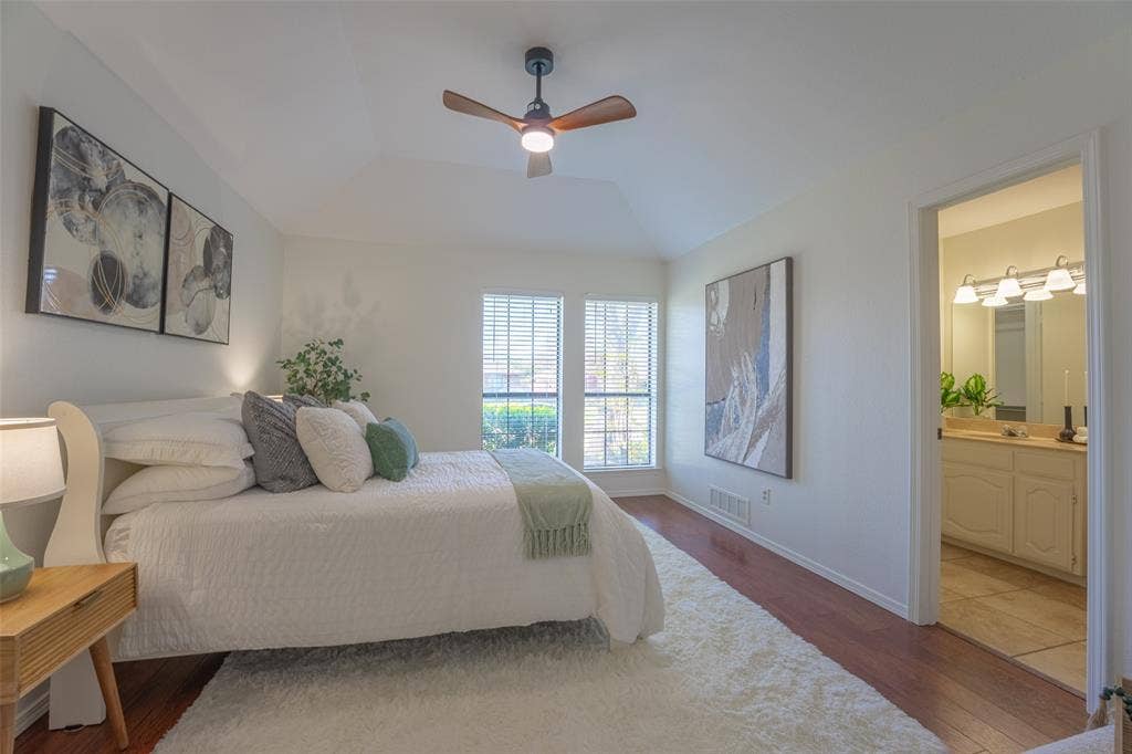 410 W Oak Street, Wylie, TX 75098 Vaulted ceiling with a ceiling fan, dual windows with blinds, wood-finish flooring, and an adjoining bathroom with a vanity and mirror