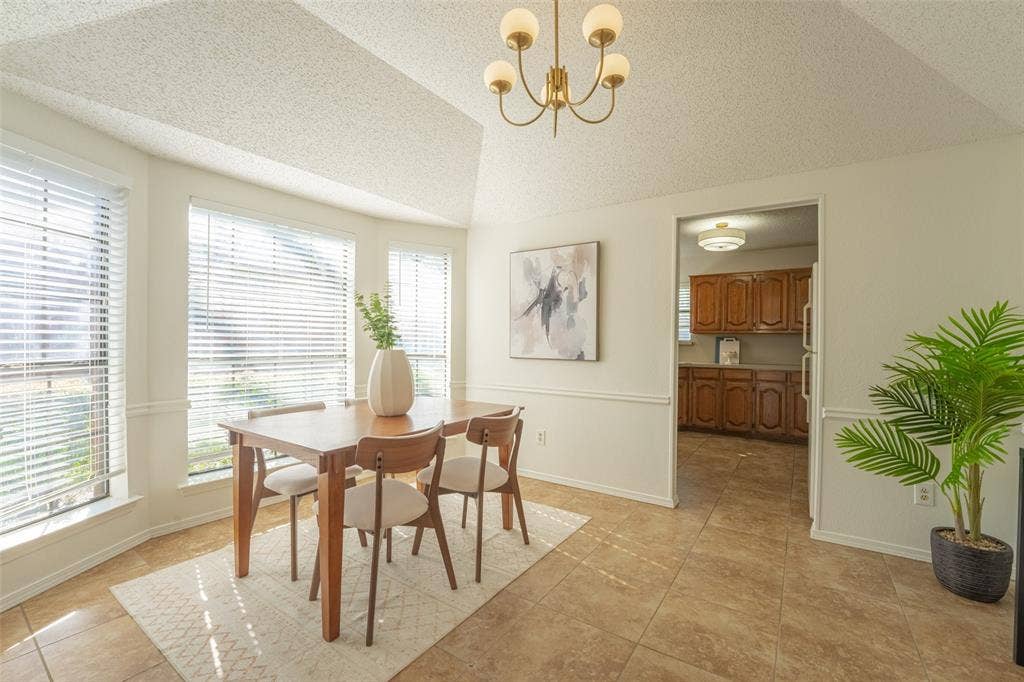 410 W Oak Street, Wylie, TX 75098 Bay window with horizontal blinds, tiled flooring, vaulted ceiling, and brass-finish chandelier