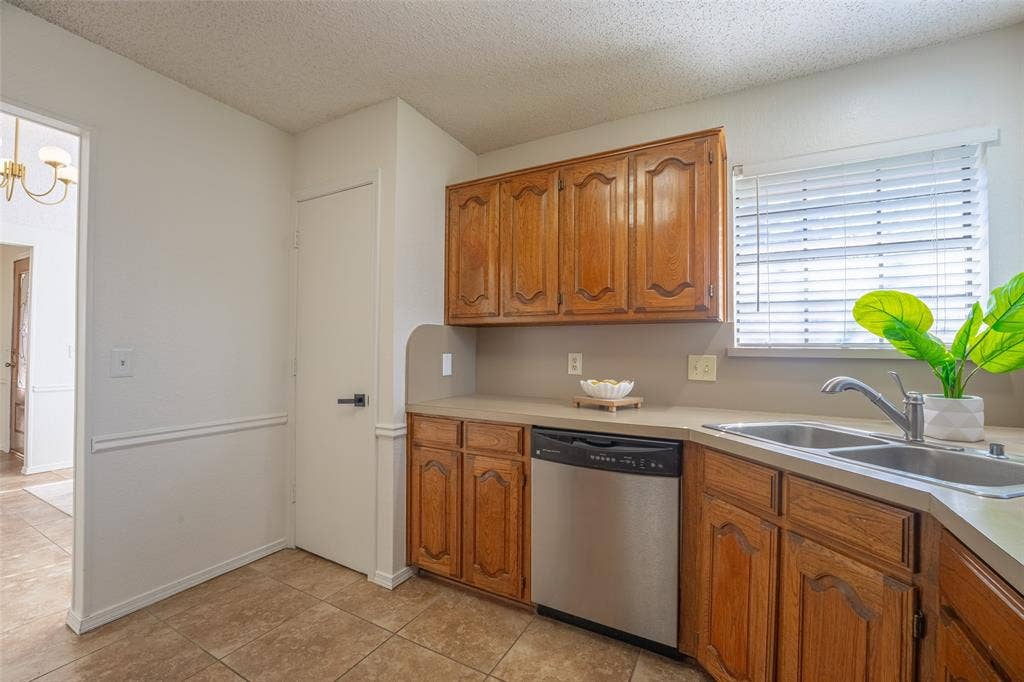 410 W Oak Street, Wylie, TX 75098 Kitchen featuring wood cabinetry, a stainless steel dishwasher, a double basin sink with a chrome faucet, light-toned countertops, and tiled flooring
