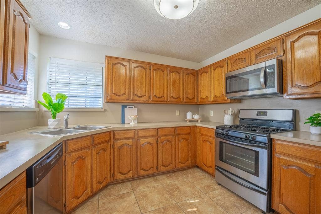 410 W Oak Street, Wylie, TX 75098 Wood-finish cabinetry, stainless steel appliances, dual basin sink, integrated dishwasher, and tiled flooring