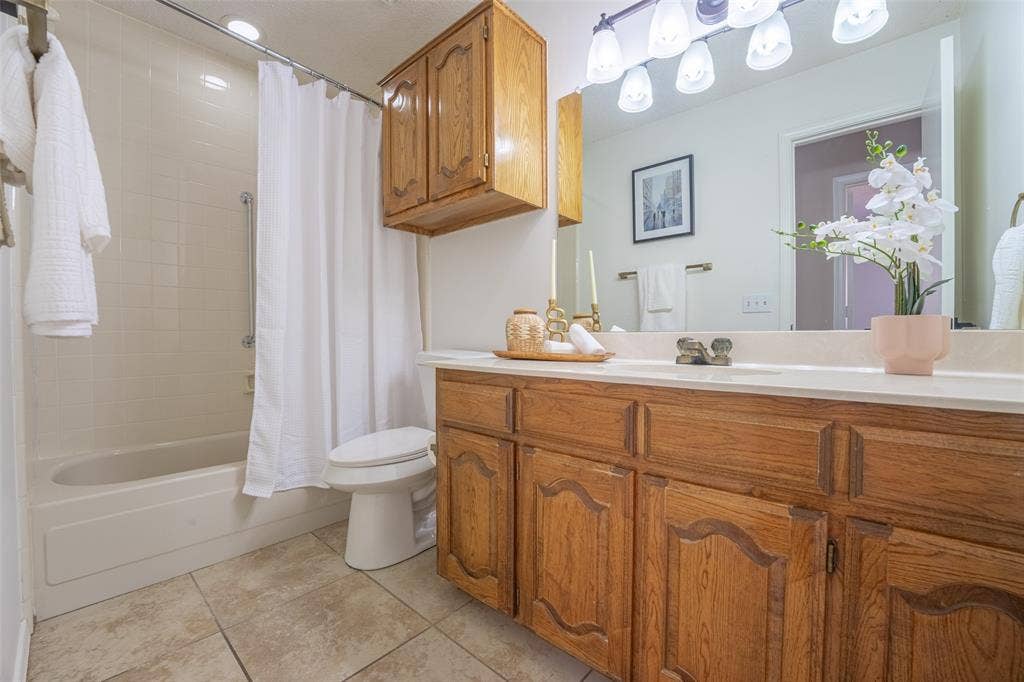 410 W Oak Street, Wylie, TX 75098 Bathroom featuring a single vanity with wood-finish cabinetry, a large wall-mounted mirror, overhead vanity lighting, a bathtub with a shower, and tile flooring