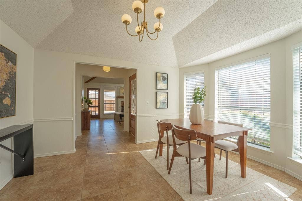 410 W Oak Street, Wylie, TX 75098 Vaulted ceiling, ceramic tile flooring, chair rail molding, bay window with blinds, and decorative chandelier