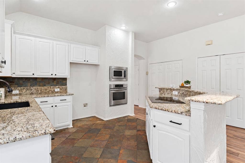 4816 Rockcreek Lane, Plano, TX 75024 Kitchen featuring granite countertops, white cabinetry with dark hardware, stainless steel built-in appliances, and multi-toned tile flooring