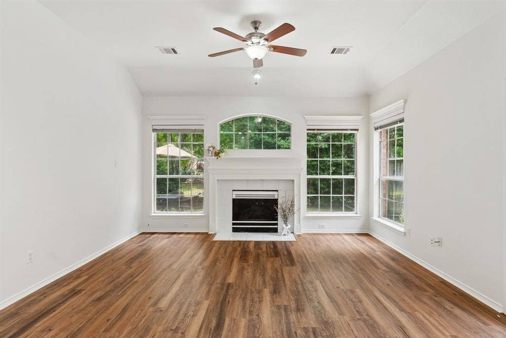 4816 Rockcreek Lane, Plano, TX 75024 Wood-finish flooring, white fireplace with hearth, arched window, and ceiling fan