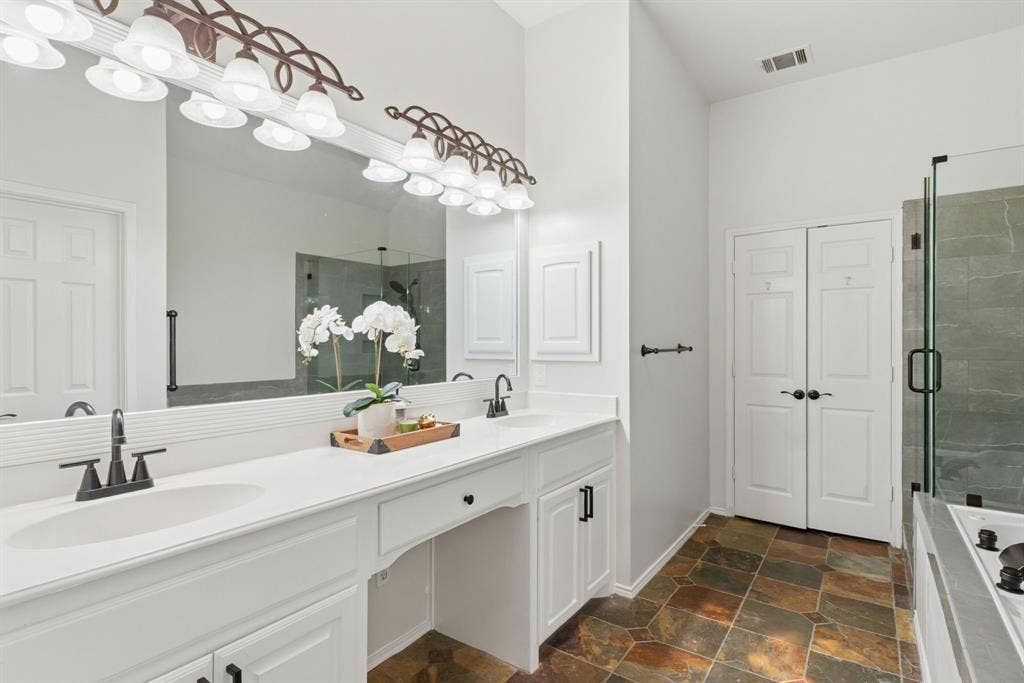4816 Rockcreek Lane, Plano, TX 75024 Dual vanity with integrated sinks and black-finish faucets, expansive framed mirror, tiled flooring, and a glass-enclosed shower with dark tile surround