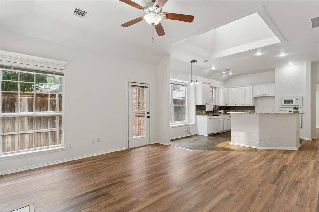 4816 Rockcreek Lane, Plano, TX 75024 Wood-finish flooring, vaulted ceiling, ceiling fan, white cabinetry, and kitchen island with a countertop