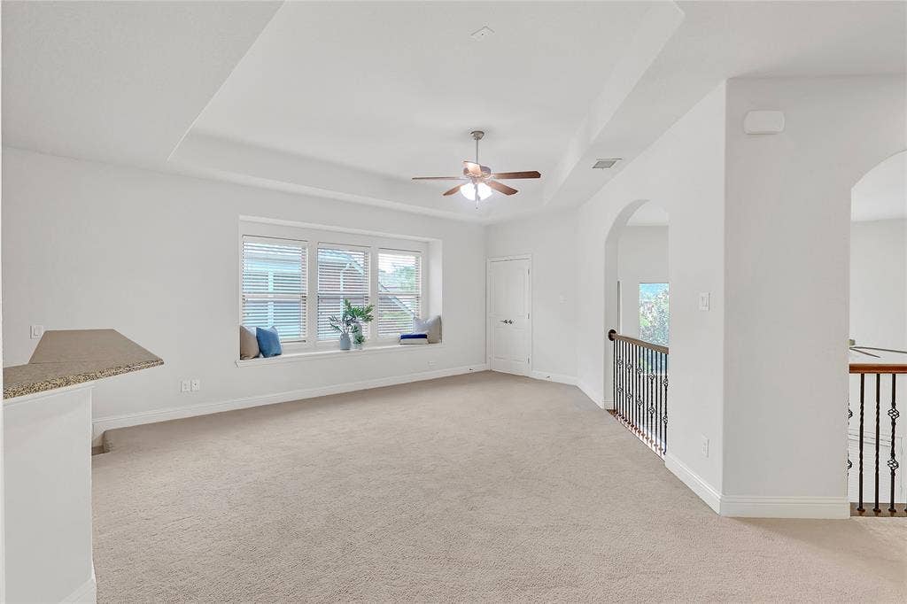 8730 Isaac Street, Plano, TX 75024 Empty room featuring arched walkways, a raised ceiling, a ceiling fan, and carpet flooring