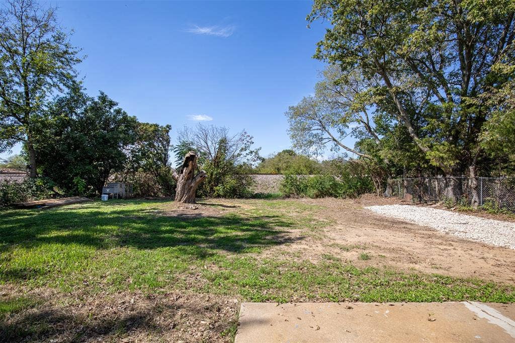 Expansive backyard featuring a partial gravel area, mature trees, and a concrete patio section