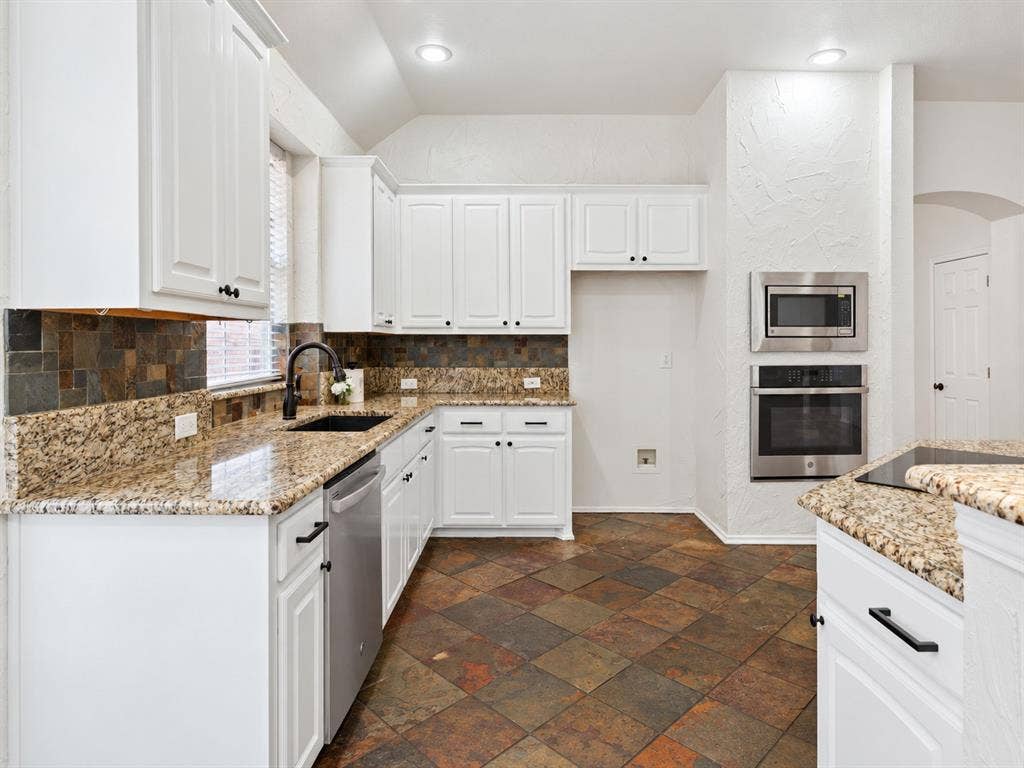 4816 Rockcreek Lane, Plano, TX 75024 White cabinetry, built-in stainless steel oven and microwave, dark bronze hardware, multi-toned tile flooring, and granite countertops