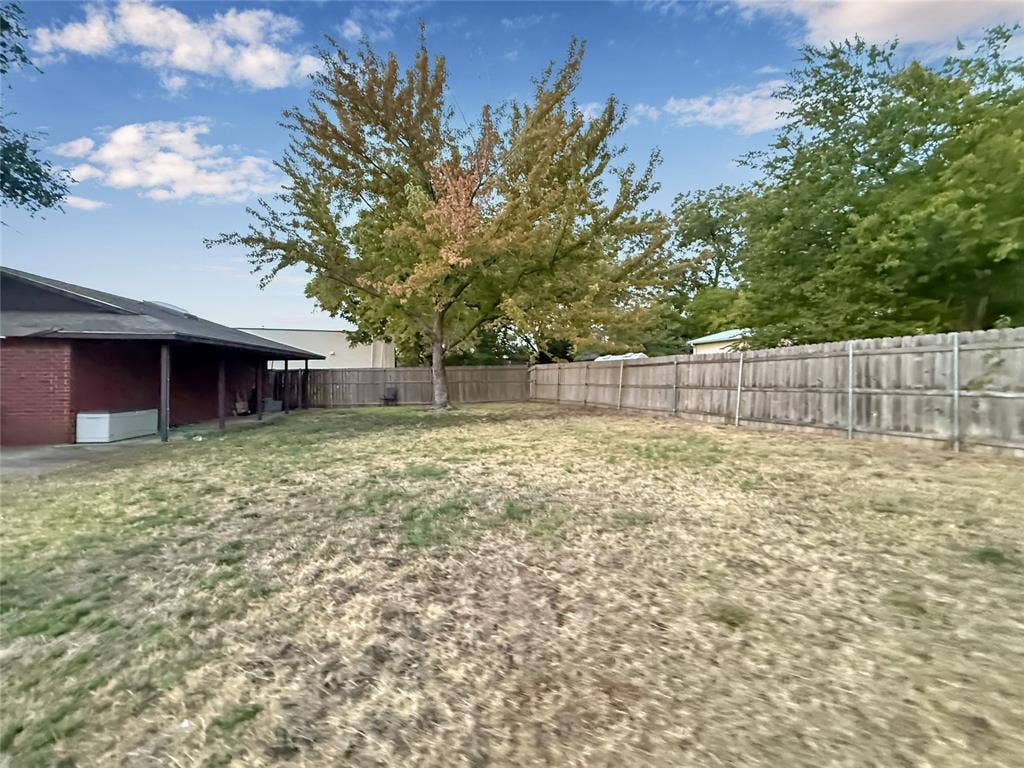 316 N Winding Oaks Drive, Wylie, TX 75098 Expansive backyard featuring a wood privacy fence, mature trees, and a covered patio with a red brick exterior
