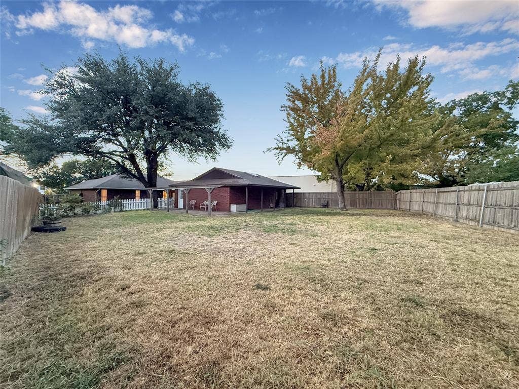 316 N Winding Oaks Drive, Wylie, TX 75098 Expansive backyard featuring a privacy fence, mature trees, and a covered patio area with a brick exterior
