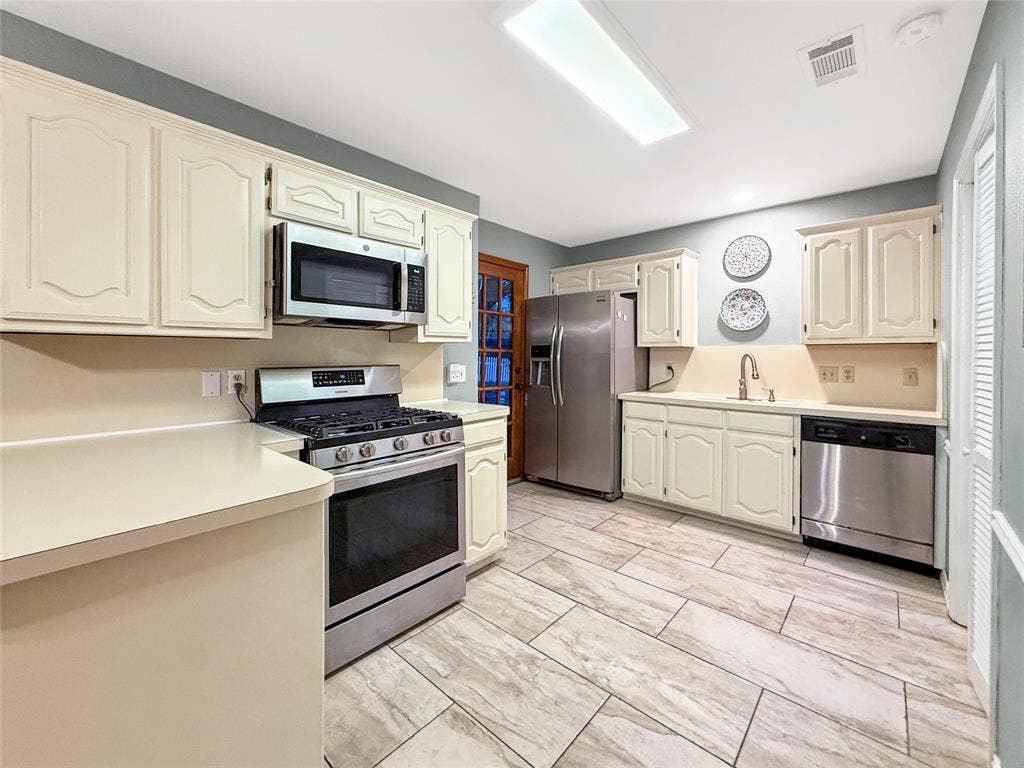 316 N Winding Oaks Drive, Wylie, TX 75098 Cream-painted cabinetry, stainless steel appliances, light-toned countertops, and rectangular tile flooring