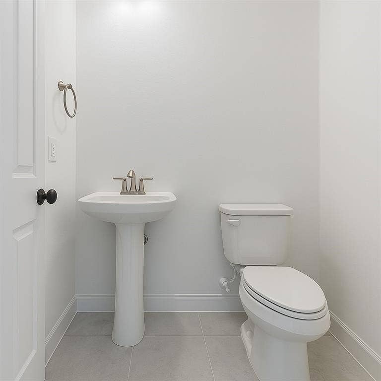 1733 Dalhart Road, Plano, TX 75075 Pedestal sink with a brushed nickel faucet, white toilet, light gray tile flooring, and a white interior door with a black knob