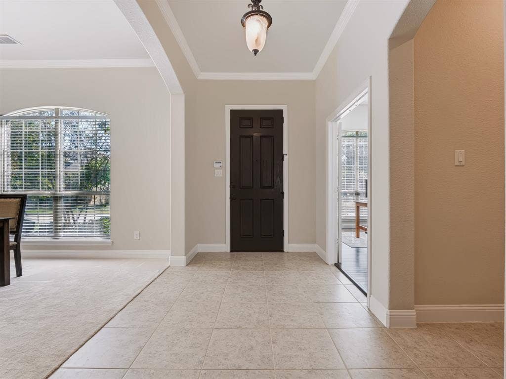 Tiled entryway with dark paneled door and crown molding