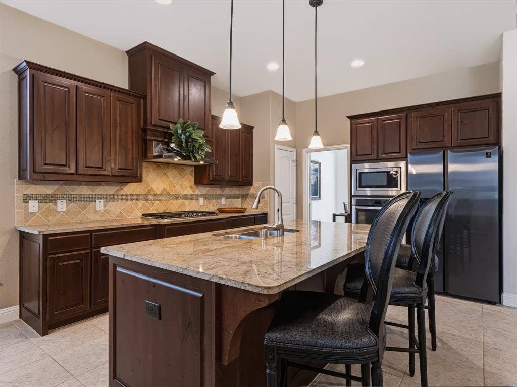 Kitchen featuring dark wood-finish cabinetry, light-toned granite countertops, stainless steel appliances, a tiled backsplash, and recessed lighting