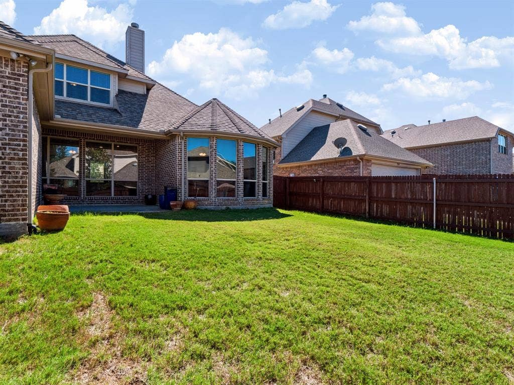 Expansive backyard featuring a manicured lawn, a full brick exterior, a large bay window, a concrete patio, and a privacy fence