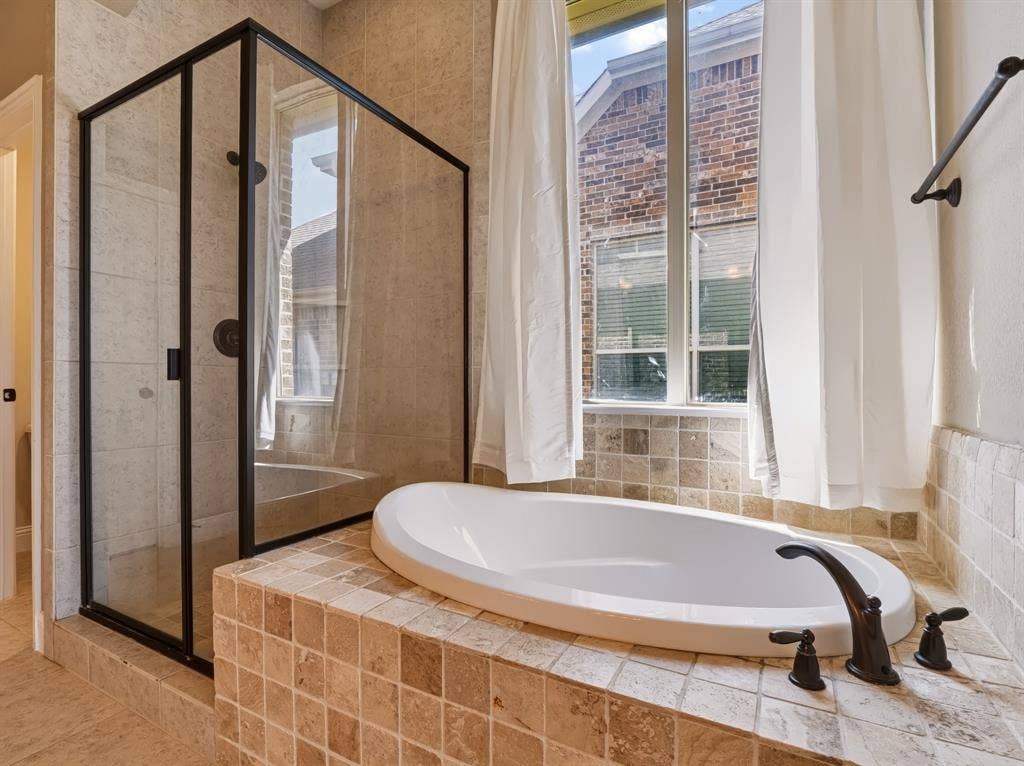 Enclosed glass shower with black framing, built-in soaking tub, and tile surround with bronze fixtures