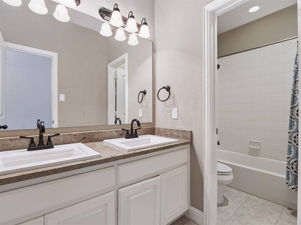 Dual vanity with white cabinetry, speckled countertop, and dark-finish faucets
