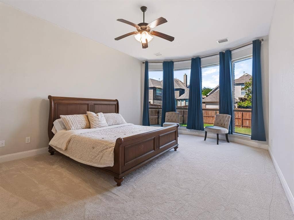 Tray ceiling with a ceiling fan, light-toned carpeting, and a bay window