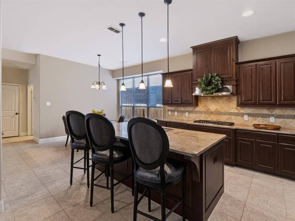 Kitchen featuring dark wood cabinetry, light-toned countertops, a tile backsplash, and pendant lighting