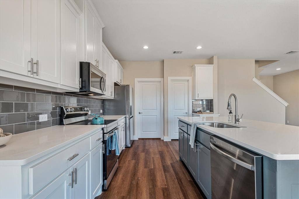 White shaker cabinetry, stainless steel appliances, solid surface countertops, gray subway tile backsplash, and wood-finish flooring
