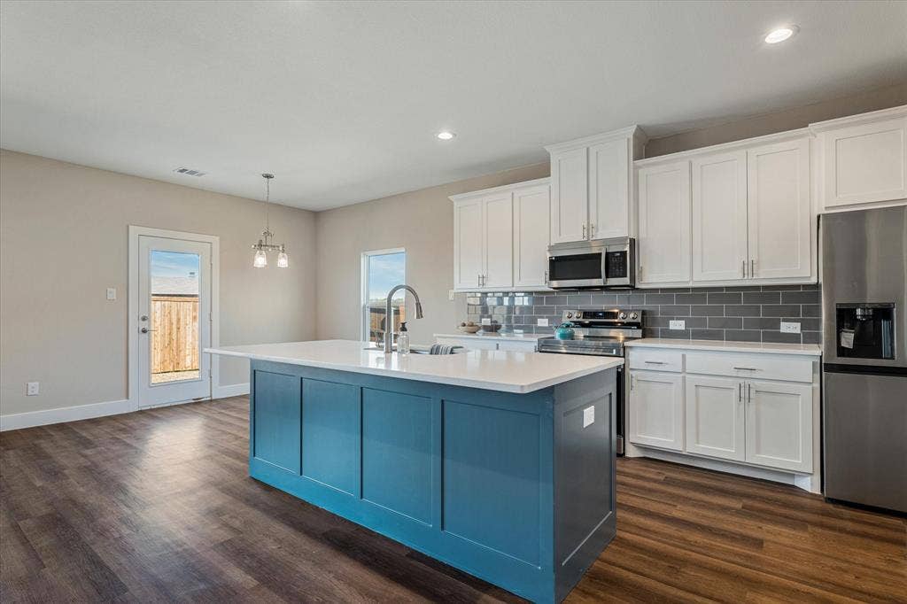 Kitchen featuring a central island with white countertop, white upper and lower cabinetry, stainless steel appliances, and a gray subway tile backsplash