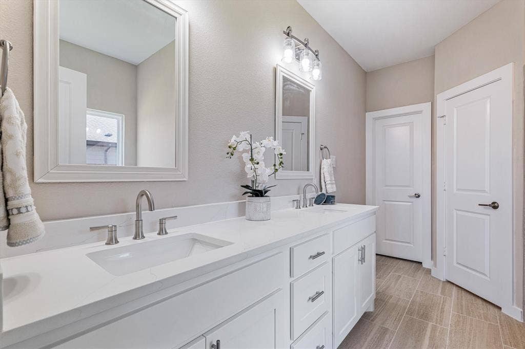 Dual vanity with integrated sinks, white cabinetry, brushed nickel hardware, and light-toned tile flooring