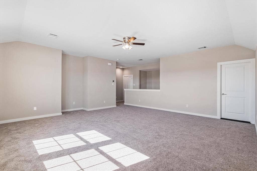 Expansive carpeted area with vaulted ceilings, a ceiling fan, and light-toned walls