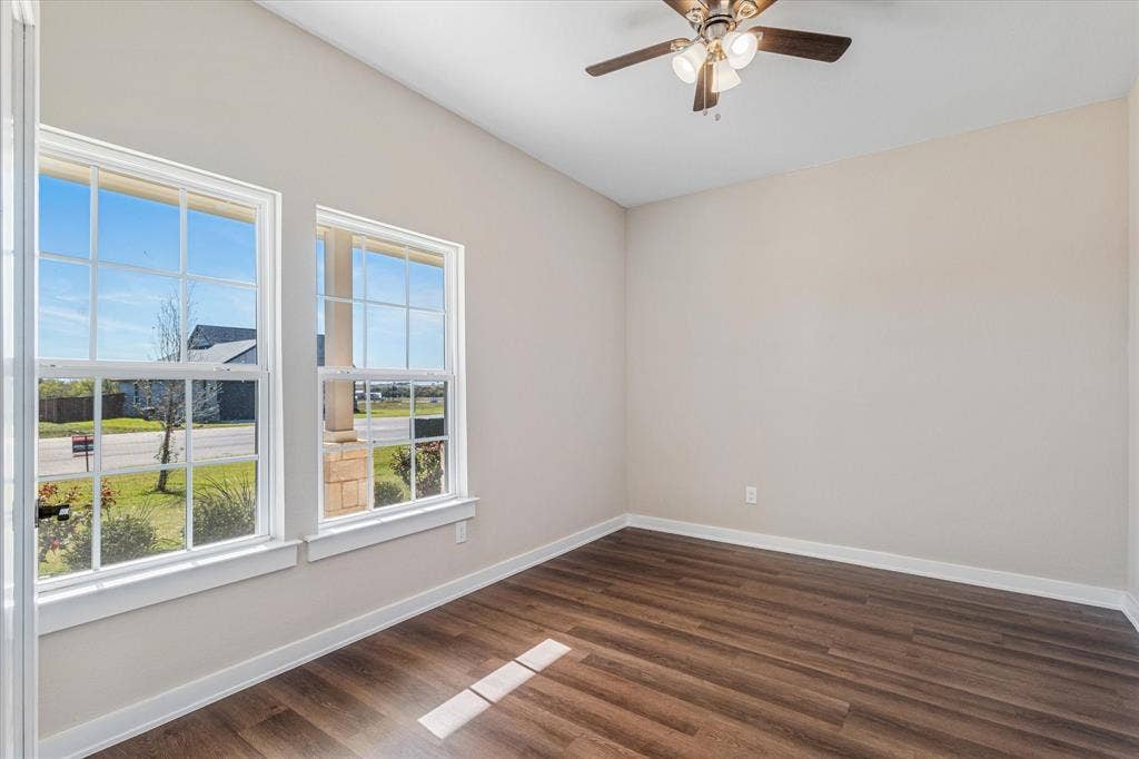 Wood-finish flooring, white trim, dual windows with grilles, and a ceiling fan with integrated lighting
