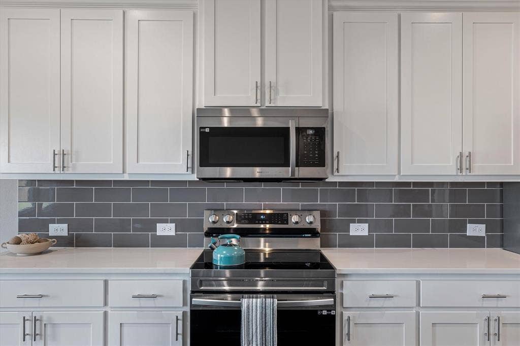 White shaker-style cabinetry, stainless steel appliances, solid surface countertops, and a gray subway tile backsplash