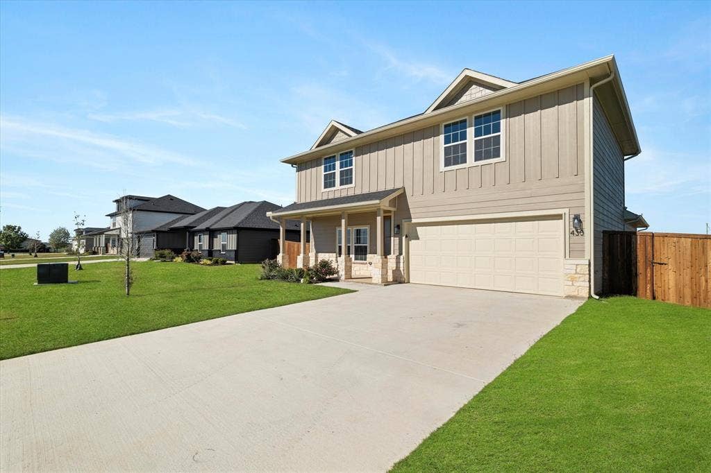 Two-story residence featuring a two-car garage, concrete driveway, and a covered front porch with stone accents