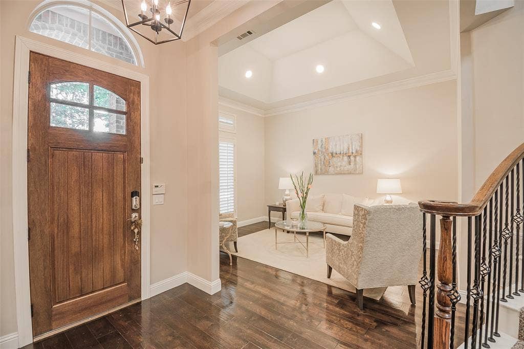 5925 Westmont Drive, Plano, TX 75093 Rich wood-finish flooring, a solid wood entry door with an arched glass panel, and an open-concept living area with a vaulted ceiling