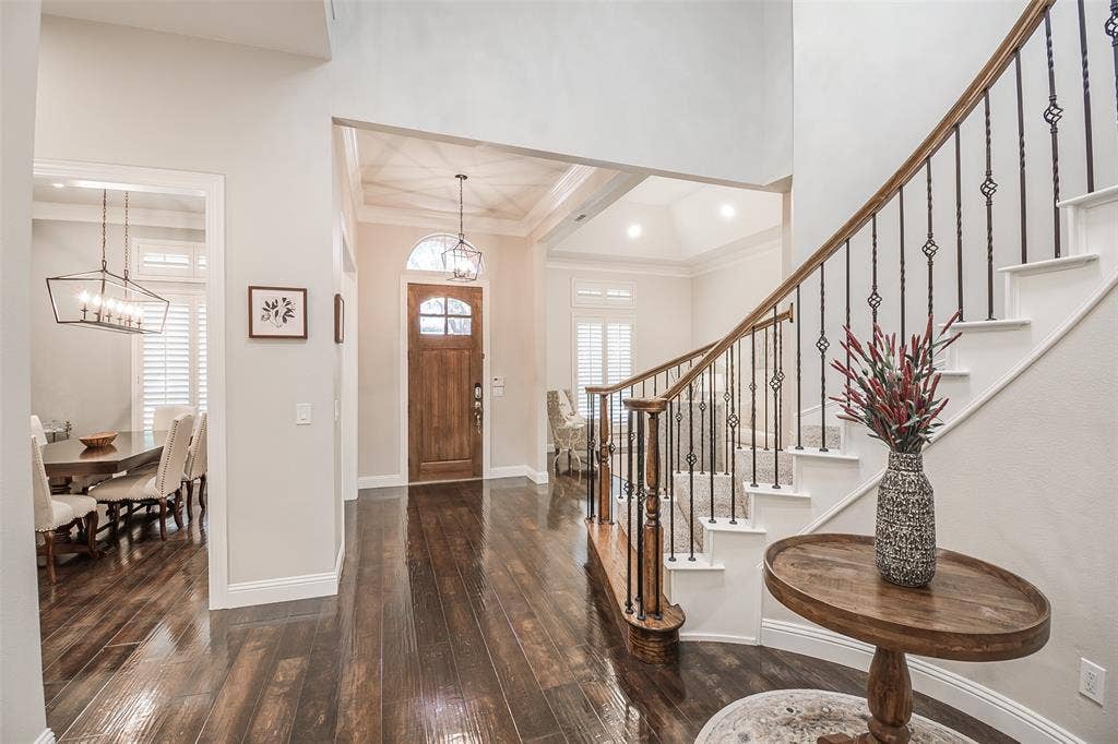 5925 Westmont Drive, Plano, TX 75093 Wood-finish flooring throughout, elegant staircase with wrought iron balusters, arched entryway, and custom wooden front door with glass inserts
