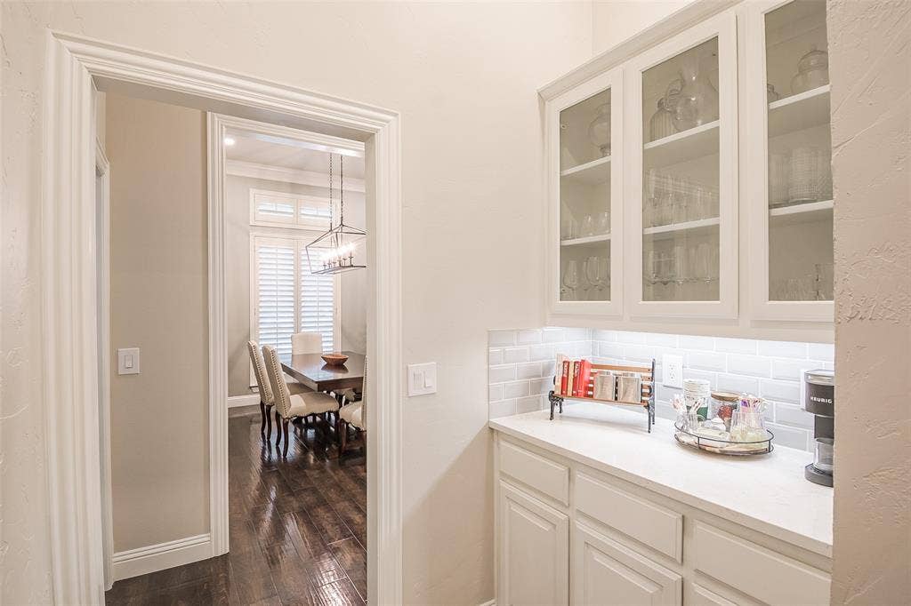 5925 Westmont Drive, Plano, TX 75093 Built-in cabinetry with glass-front uppers, white countertop, white subway tile backsplash, and dark wood-finish flooring