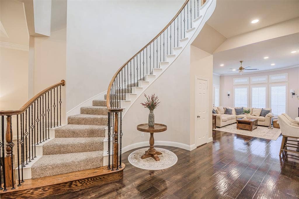 5925 Westmont Drive, Plano, TX 75093 Sweeping staircase with wrought iron balusters and wood handrails, wood-finish flooring, recessed lighting, and a living area featuring window shutters