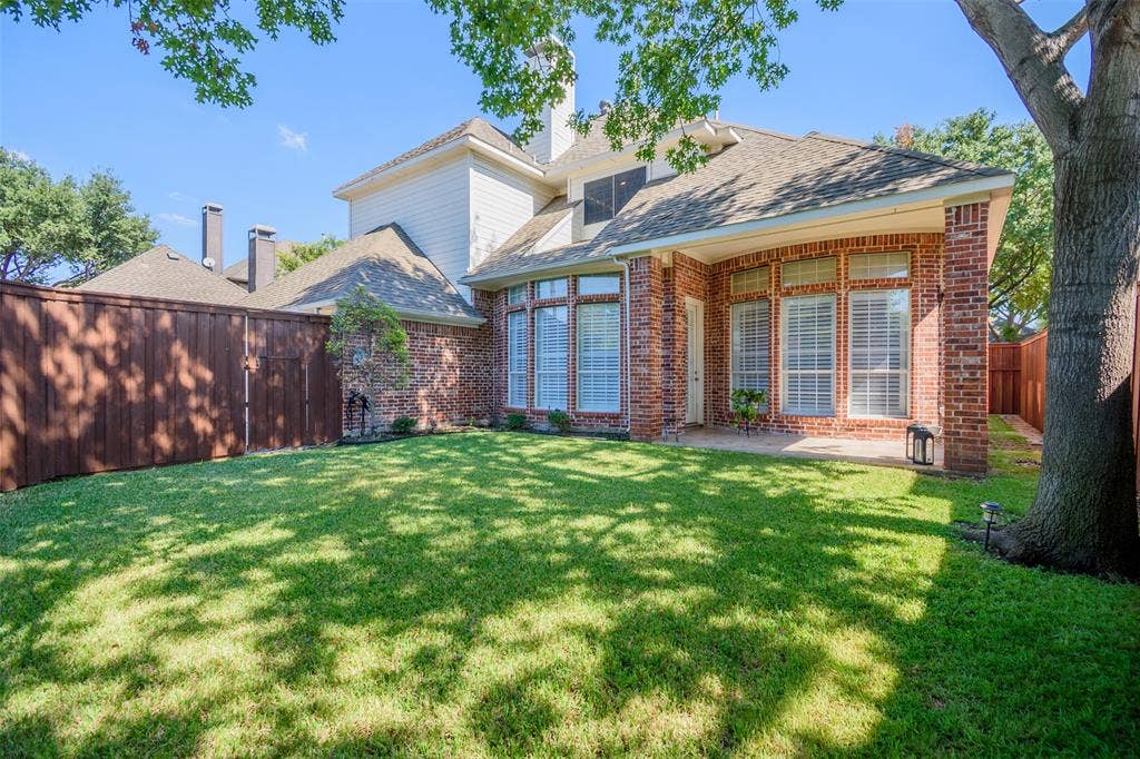 5925 Westmont Drive, Plano, TX 75093 Expansive backyard featuring a manicured lawn, brick exterior, bay windows with shutters, and a covered patio