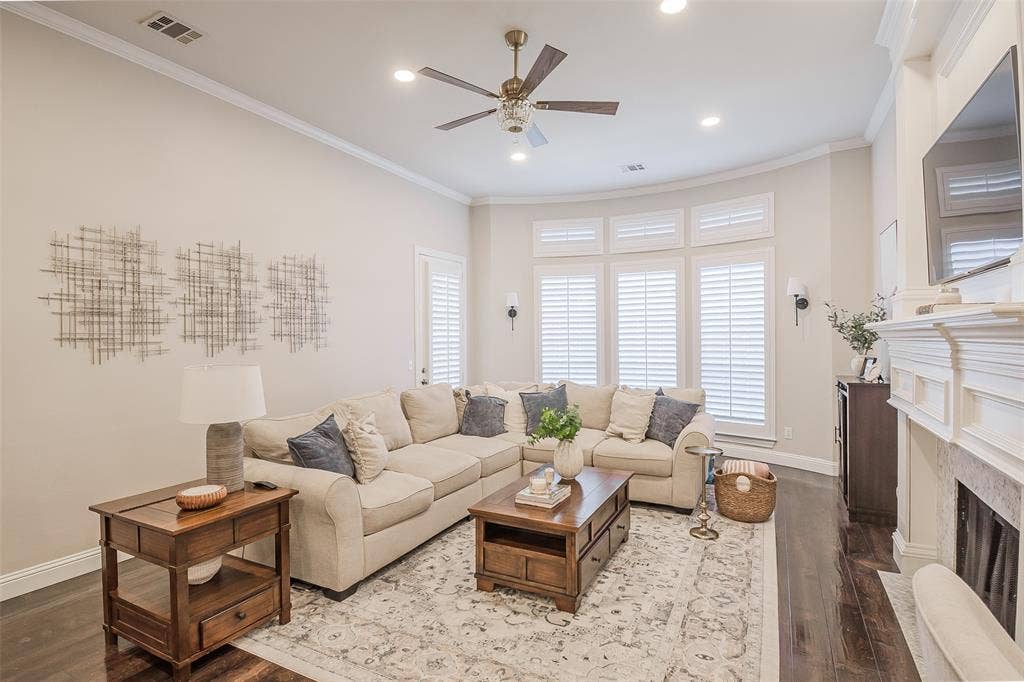5925 Westmont Drive, Plano, TX 75093 Spacious living area featuring dark wood-finish flooring, a decorative fireplace, and large windows with plantation shutters