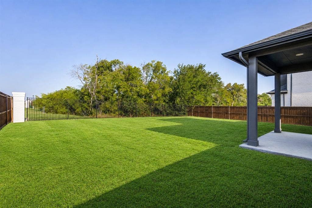 2902 Cremini Fls, Princeton, TX 75407 Expansive lawn with a covered concrete patio, wood privacy fencing, and a black wrought iron fence